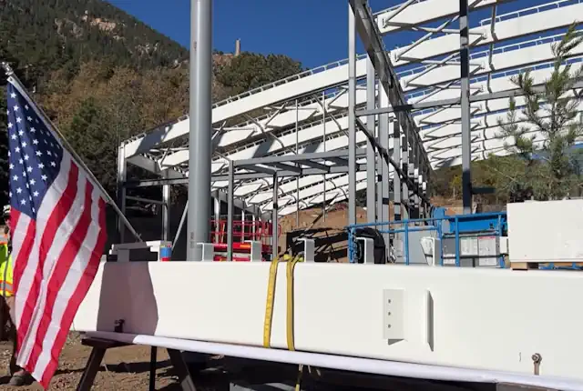Celebrating placement of the last beam on the new giraffe enclosure at Cheyenne Mtn Zoo a tree and American Flag are hoisted to the top of the building.